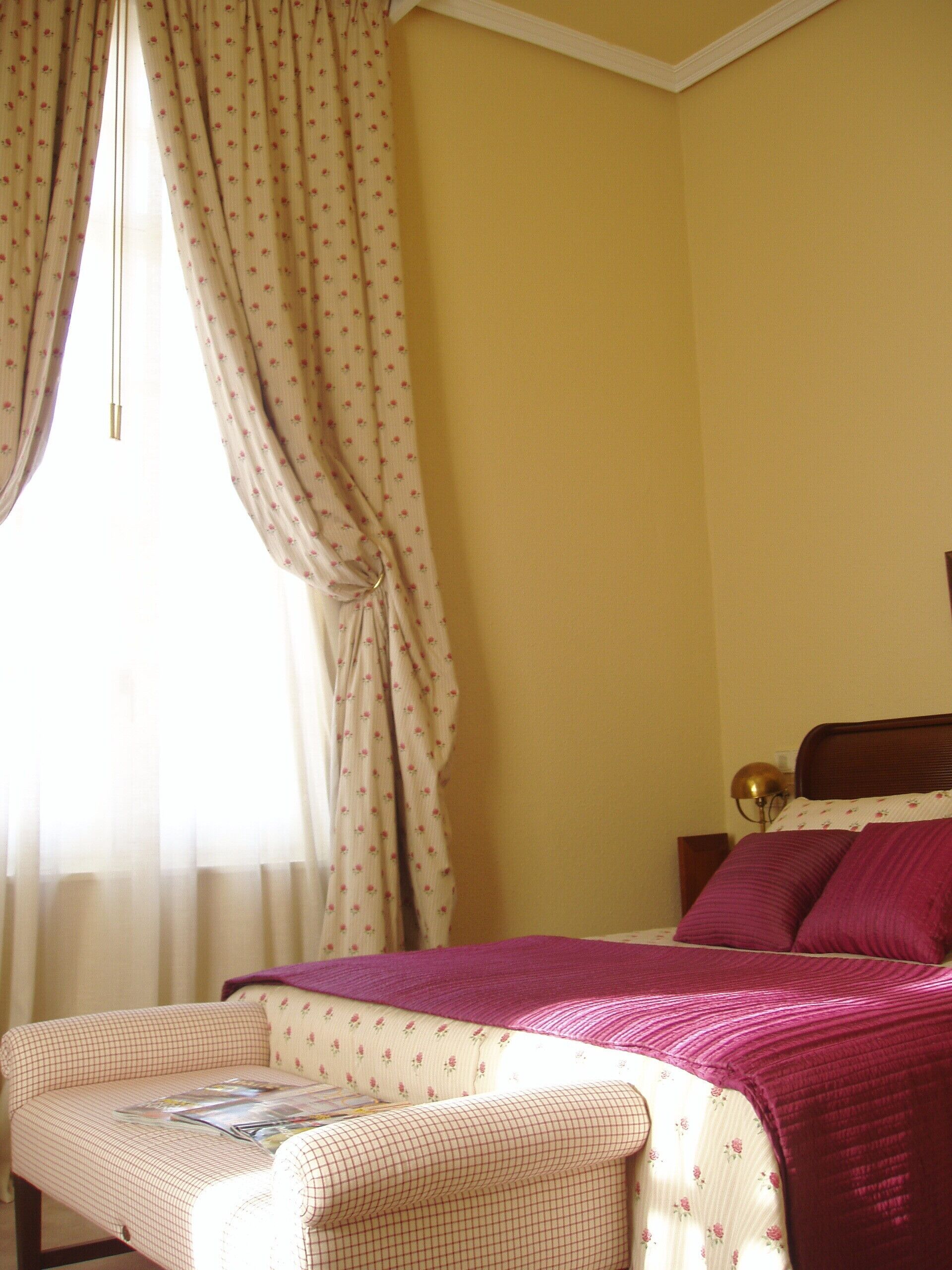 Un dormitorio con cama, mesita de noche, lámpara y ventana con cortinas.