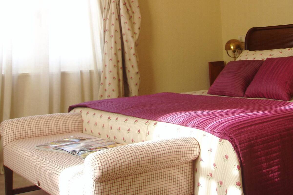 A bedroom with a bed, a bedside table, a lamp, and a window with curtains.