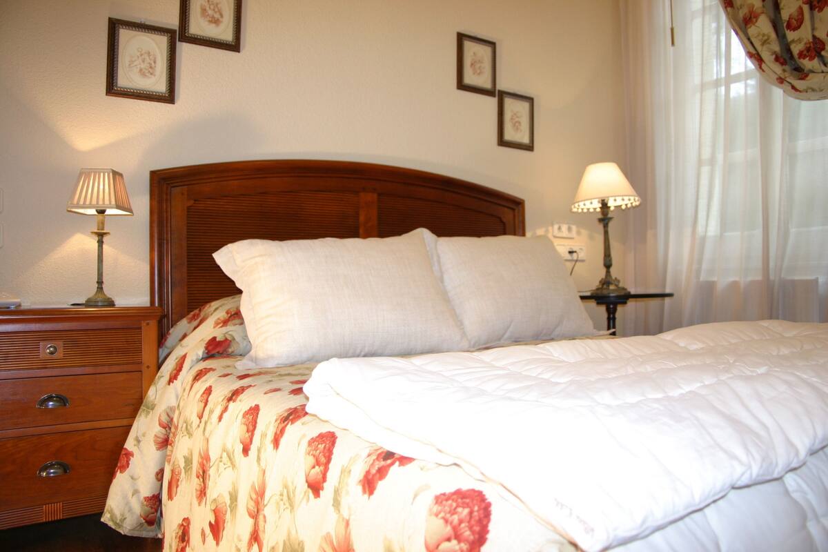 A neatly made bed with a floral bedspread, a wooden headboard, and two bedside lamps.