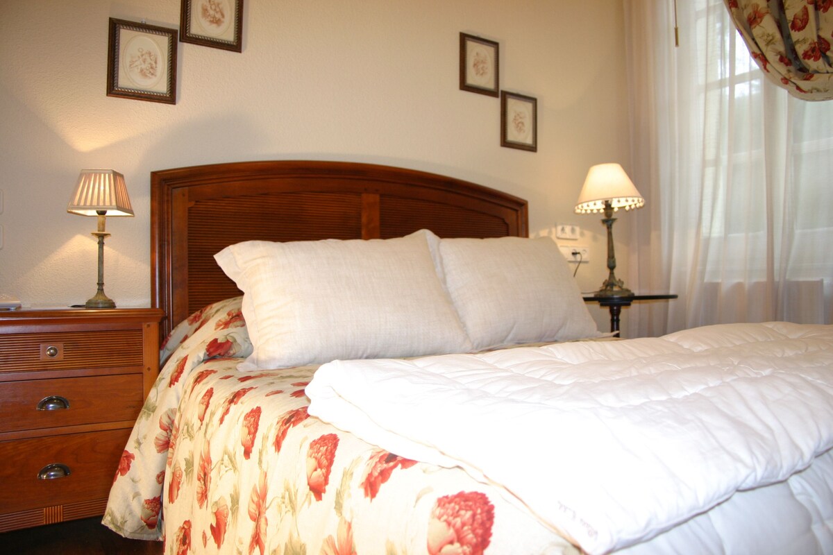 Un lit bien fait, avec une couvre-lit à motifs floraux, une tête de lit en bois et deux lampes de chevet.