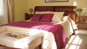 Una cama bien hecha con una manta y almohadas rosas, una mesita de noche con lámpara, y un cuadro enmarcado en la pared.