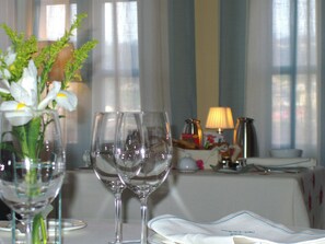 Una mesa con dos copas de vino vacías, un jarrón con flores y una lámpara sobre un mantel.