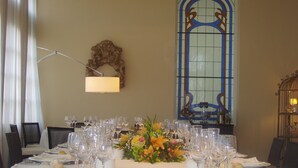 A dining table set for a formal meal with multiple wine glasses and plates, a floral centerpiece, and a stained glass window in the background. - Hotel Arcea Palacio de las Nieves (Oviedo)