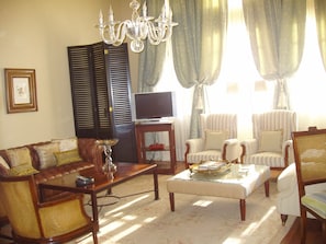 Un salon comprenant un canapé, des fauteuils, une table basse, un téléviseur et un lustre.