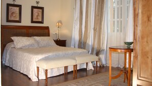 A bedroom with a large bed, a bedside table with a lamp, a wooden bench, and a small table with a bowl. - Hotel Arcea Palacio de las Nieves (Oviedo)