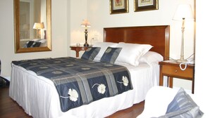 Una cama bien hecha con colcha de estampado floral, cabecera de madera y mesita de noche con lámpara y teléfono.