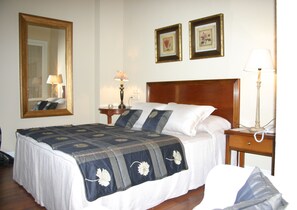 A neatly made bed with a floral-patterned bedspread, a wooden headboard, and a nightstand with a lamp and phone. - Hotel Arcea Palacio de las Nieves (Oviedo)