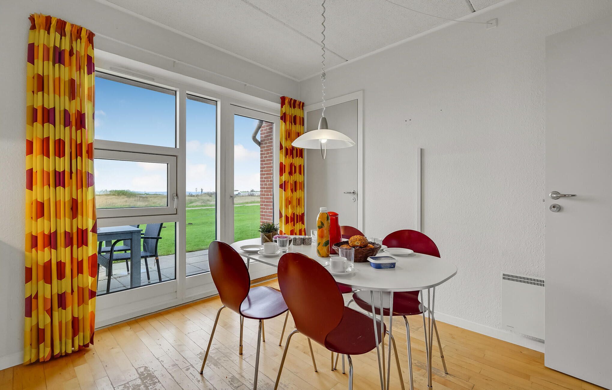 A dining area with a table set for four, a view of the outdoors, and a door leading to another room.