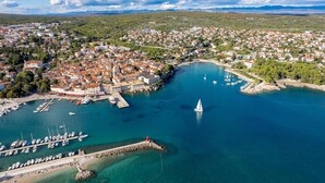 Vista aérea de un pueblo costero con un puerto deportivo, aguas azules cristalinas y un faro.