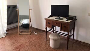 Ein Zimmer mit Schreibtisch aus Holz, Fernseher, Spiegel, Heizkörper und Steckdose.