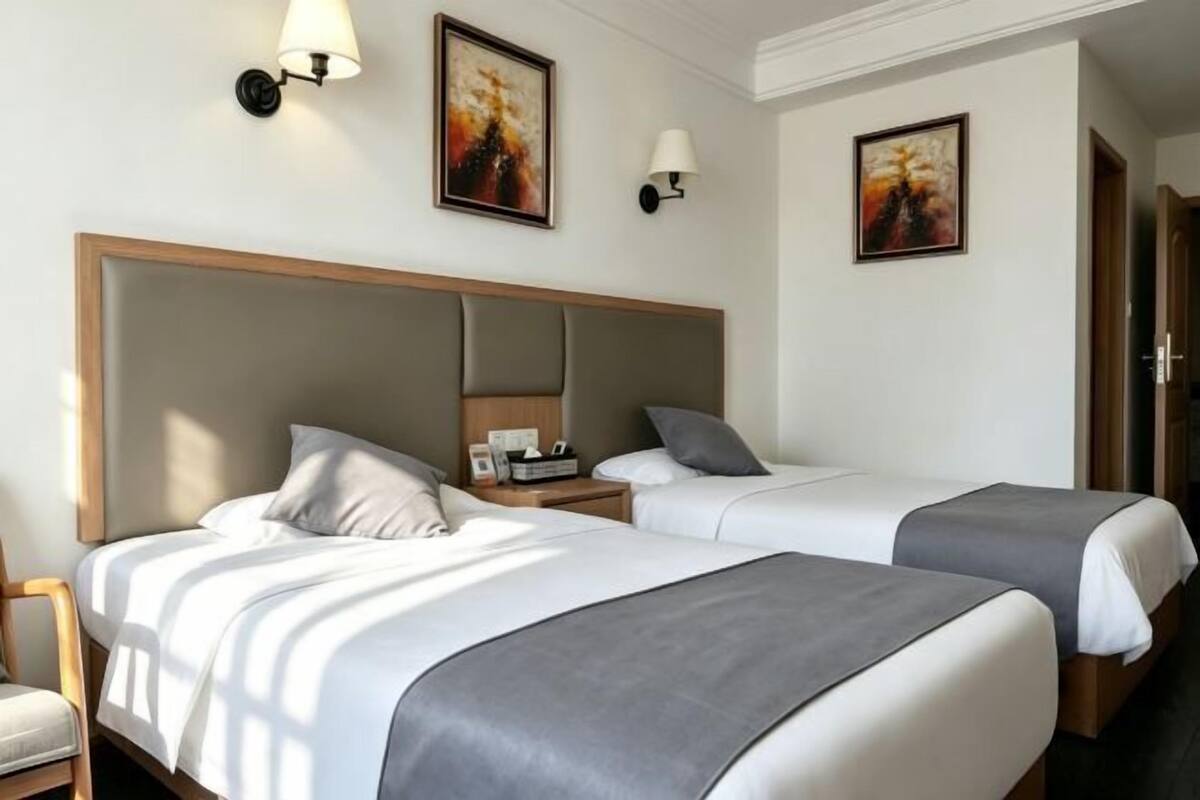 A hotel room with two beds, a wooden headboard, bedside lamps, and abstract paintings on the walls.