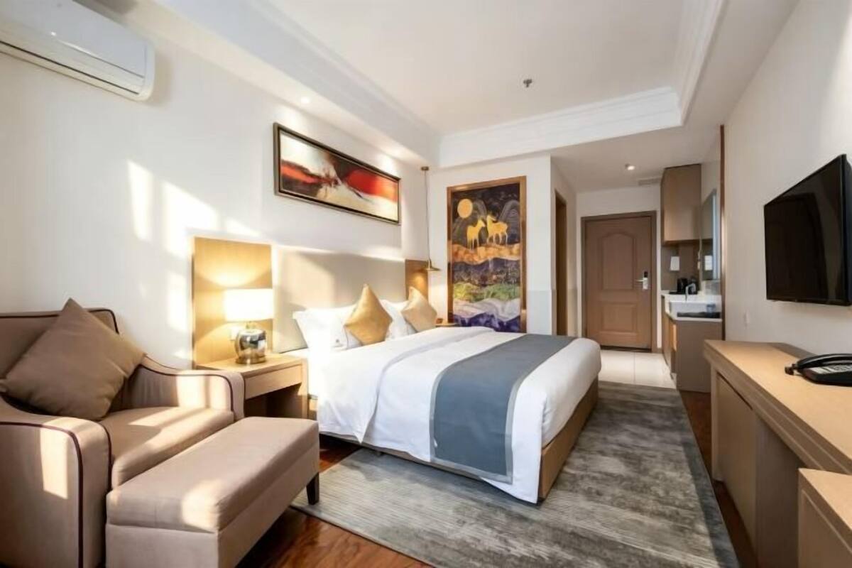 A hotel room with a bed, a desk, a chair, a TV, and artwork on the walls.