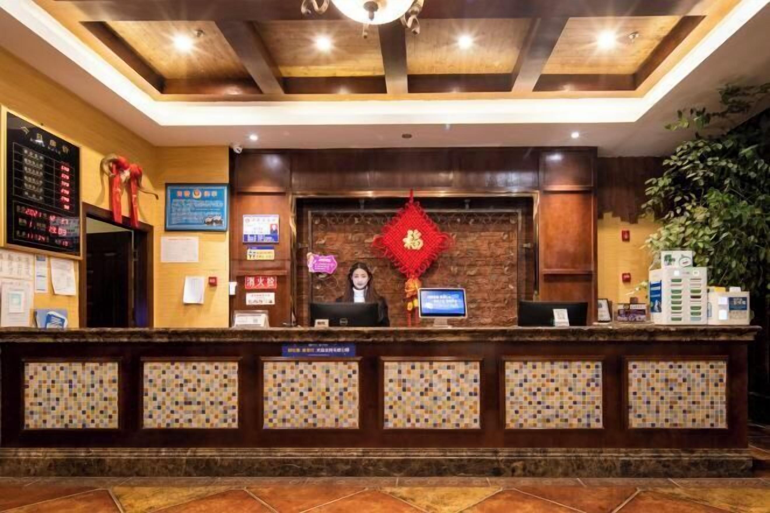 Un espace d’accueil d’hôtel avec un comptoir de réception en bois, un écran numérique et une décoration murale rouge.