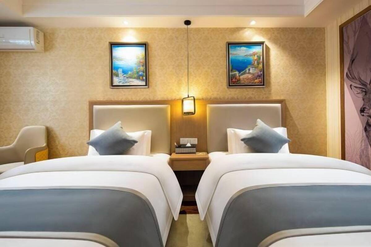 A hotel room with two beds, a nightstand with a lamp, and two framed pictures on the wall.