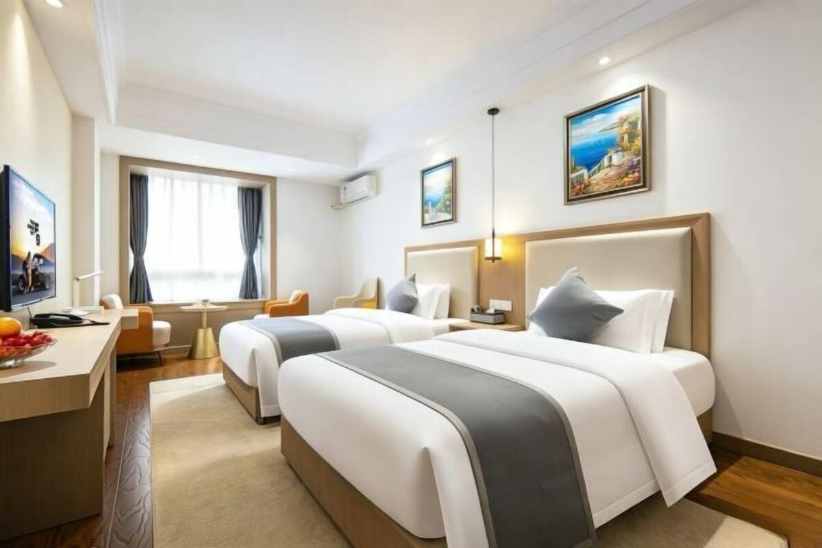 A hotel room with two beds, a desk, a TV, and a painting on the wall.