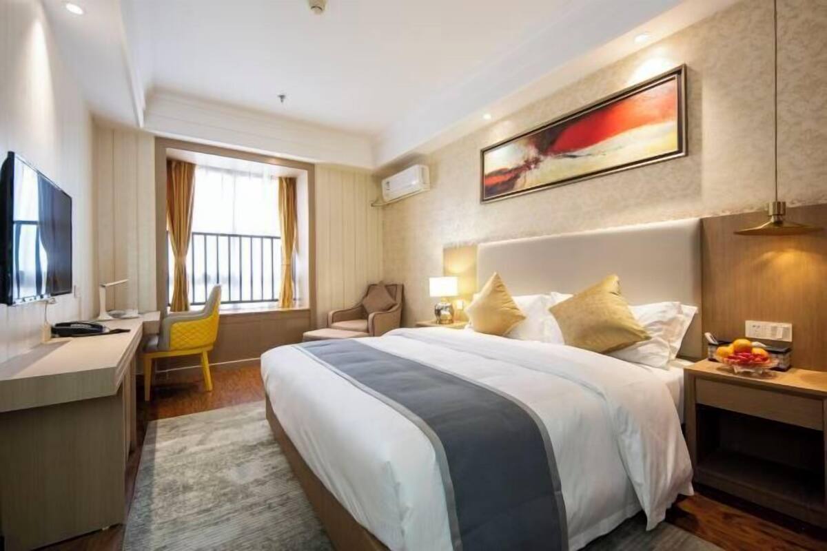 A hotel room with a bed, a desk, a chair, a TV, and a window with curtains.