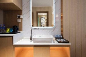 Un baño moderno con un lavamanos blanco, un espejo y un mueble de tocador de madera.