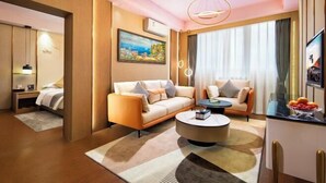 Une chambre d’hôtel moderne, équipée d’un canapé, d’une table basse ronde, d’un téléviseur et d’un tableau au mur.
