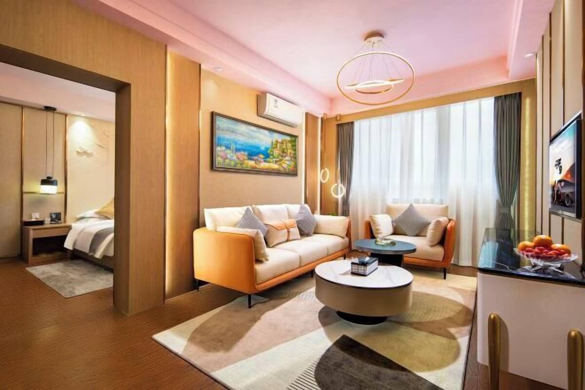 A modern hotel room with a sofa, a round coffee table, a TV, and a painting on the wall.