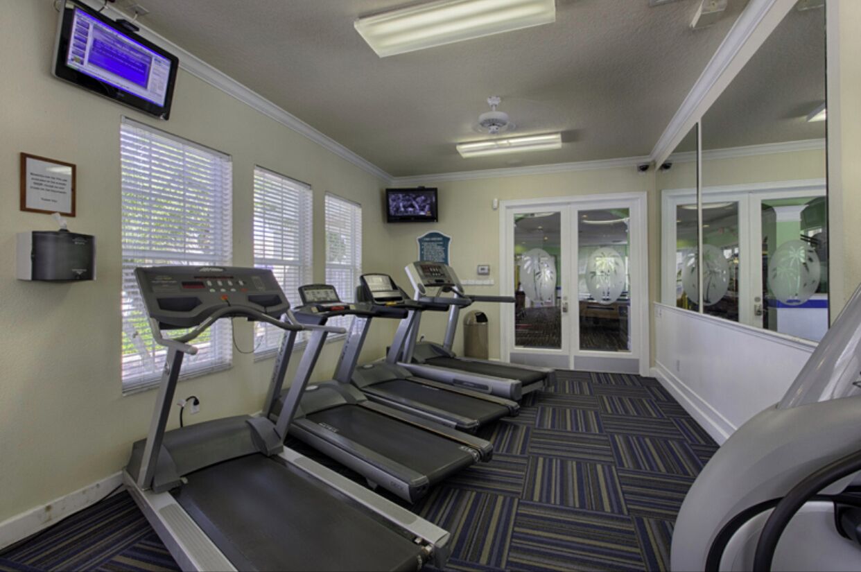 A fitness room with treadmills, a television, and a large mirror.