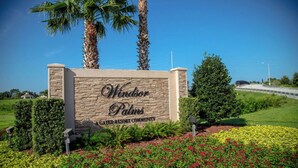 Een bord met daarop Windsor Palms, een gated resort gemeenschap, met een stenen muur en palmbomen op de achtergrond.
