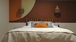 A neatly made bed with a white comforter and a single orange throw pillow, a wooden headboard, and two hanging light fixtures.