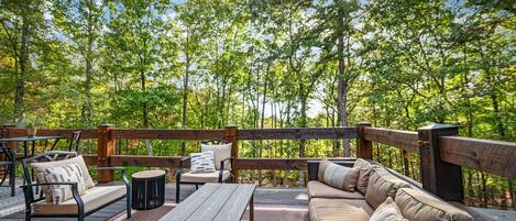 A wooden deck with outdoor furniture, including a sofa, chairs, and a table, surrounded by a wooden railing.