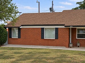 A single-story brick house with a flat roof, numbered 8021, featuring two windows with shutters, a front door, and a small front yard with grass and two potted plants. - Golden Green (Midland)