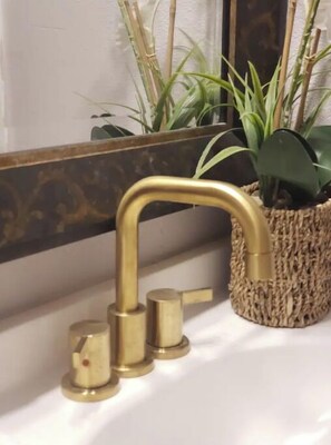 A bathroom with a gold faucet, a white sink, and a woven basket with plants. - Golden Green (Midland)