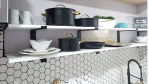 Une cuisine avec des armoires blanches, un dosseret de carreaux hexagonaux et des ustensiles de cuisine noirs rangés sur des étagères.