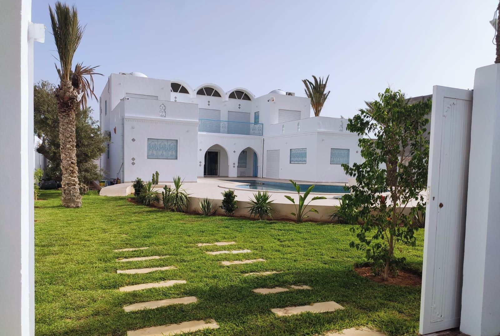 A white building with a pool, surrounded by a well-maintained lawn and palm trees.