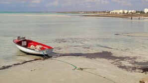 Un bateau sur une plage de sable, avec une eau claire et un ciel partiellement nuageux.