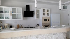 Une cuisine moderne avec des meubles blancs, un îlot central doté d’une façade en pierre, une hotte noire et un réfrigérateur blanc.