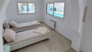 Une pièce dotée d’un plafond voûté, de deux lits avec des têtes de lit, d’une petite table et de deux fenêtres grillagées.