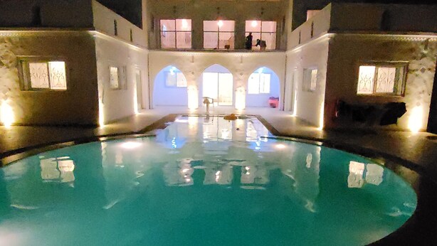Une piscine avec vue sur un bâtiment doté de fenêtres en arc de cercle et d’un balcon.