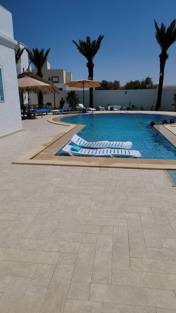Relax by the clear pool surrounded by lounge chairs and umbrellas.