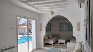 Un salon spacieux avec vue sur la piscine, des murs blancs et un coin salon confortable.
