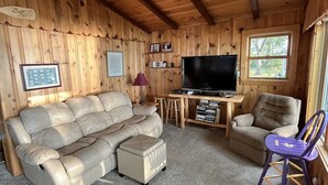 A wooden interior with a sofa, a television, a small table, and a chair. - Experience Pokegama charm in our cozy 3 bedroom cabin. (Grasston)