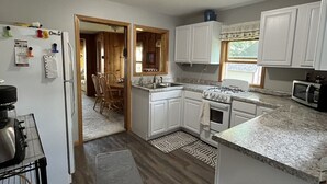 A compact kitchen with white cabinets, a built-in oven, and a microwave. There's a small rug on the floor and a trash bin in the corner. - Experience Pokegama charm in our cozy 3 bedroom cabin. (Grasston)