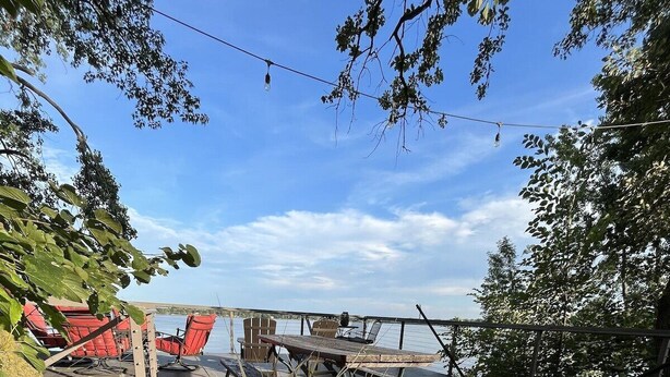 A wooden deck with a view of the water, surrounded by greenery and purple flowers. - Experience Pokegama charm in our cozy 3 bedroom cabin. (Grasston)