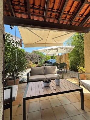 Un espace extérieur aménagé en terrasse, avec une table en bois, un canapé beige et des plantes en pot.