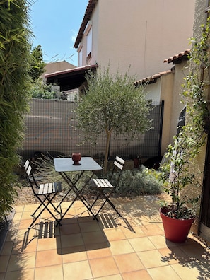 An outdoor patio with a table and chairs, surrounded by a fence and potted plants.