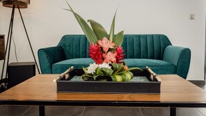 Ein Holztisch mit einer schwarzen Tablett, auf dem ein Blumenarrangement und ein Buch liegen. Im Hintergrund steht ein türkisfarbenes Sofa.