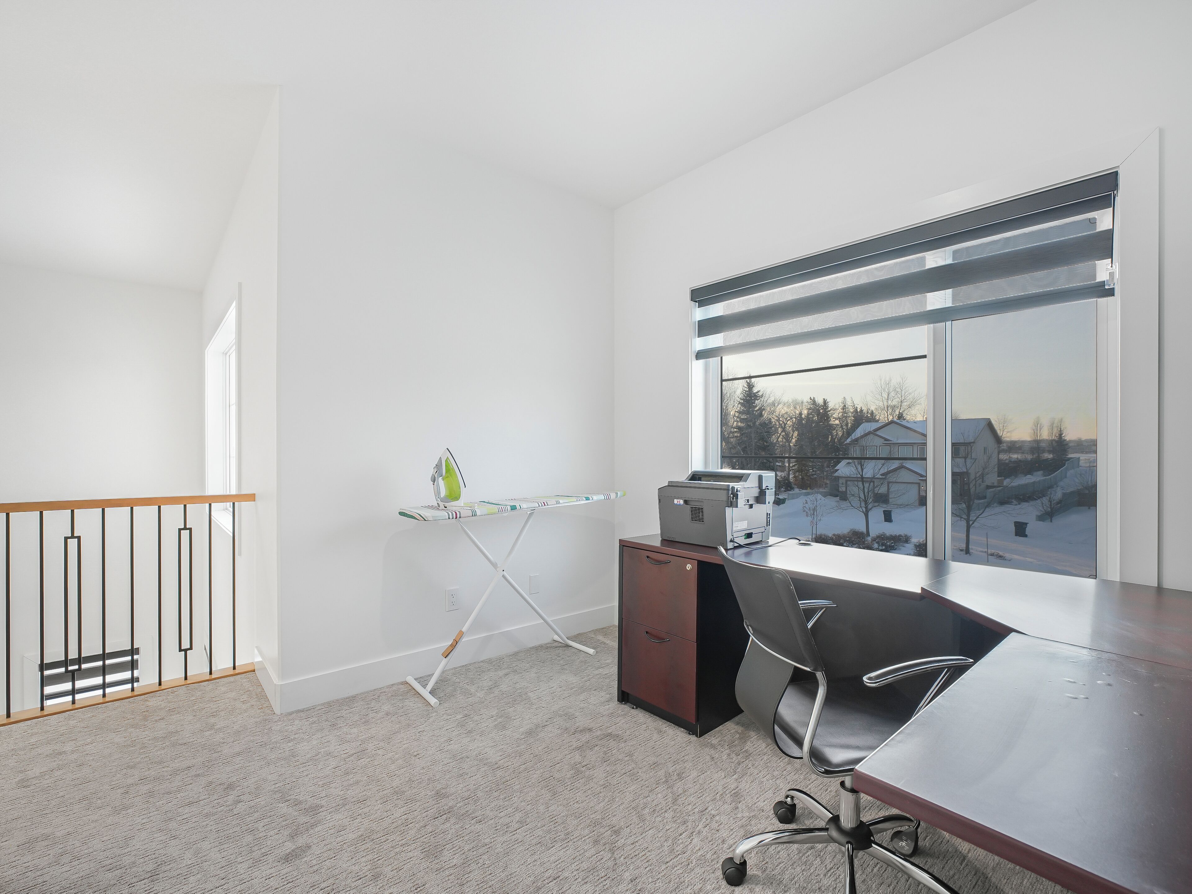 A modern office space with a desk, chair, and ironing board.