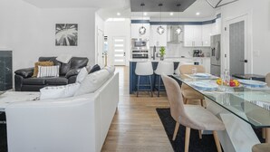 A modern living room with a sofa, a dining table with chairs, and a kitchen area with appliances.