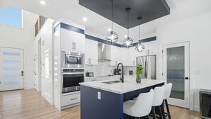 A modern kitchen with white cabinets, stainless steel appliances, a central island with bar stools, and pendant lighting.