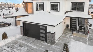 A two-story house with a garage, a covered porch, and a snow-covered roof.