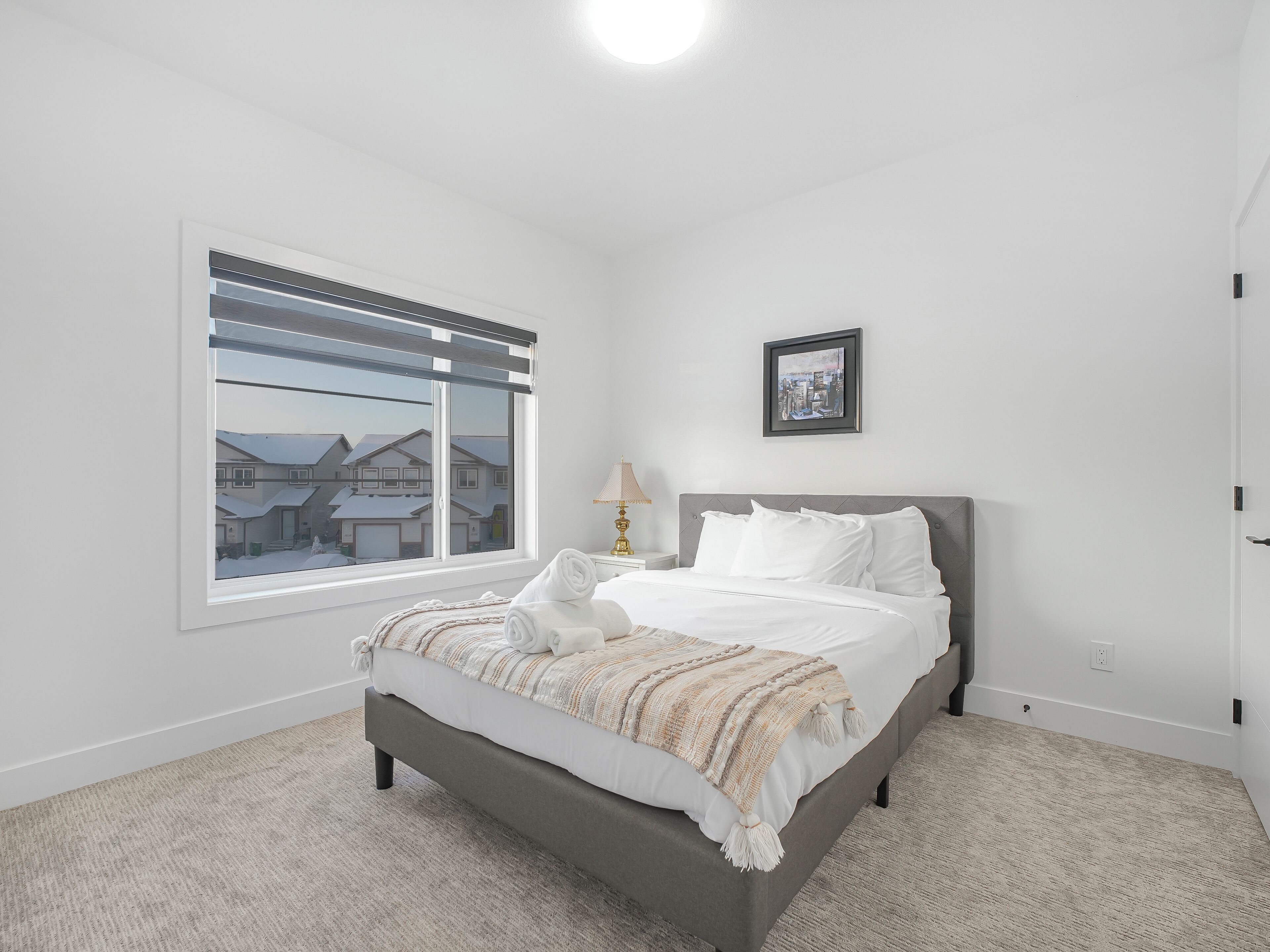 Quarto com cama, janela, luminária e quadro na parede.