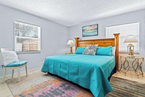 A bedroom with a bed, two bedside tables, a chair, and a window with blinds.