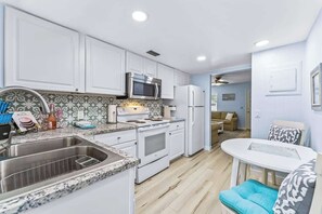 A compact kitchen with white cabinets, a stainless steel sink, a microwave, and a refrigerator.